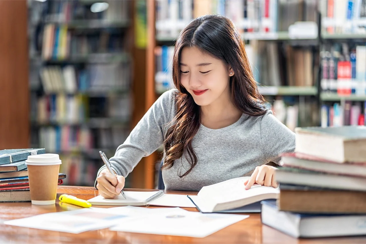 Young woman studying in a library with books and notes, symbolizing focused exam preparation.